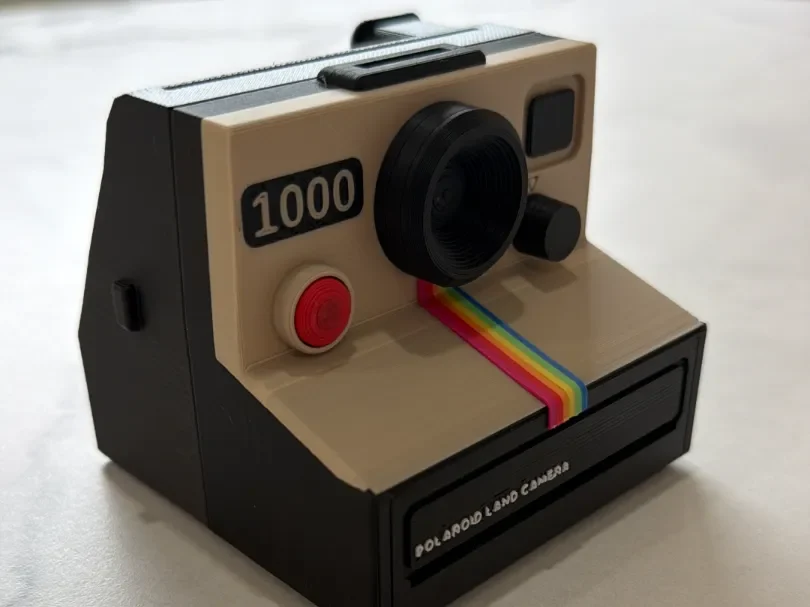 A photo of the actual printed model: cream face, black body, red shutter button, rainbow stripe, '1000' badge.